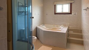 A modern bathroom with a glass-enclosed shower, a freestanding bathtub, and a window with a view. - Golden Eagle/ jacuzzi/WIFI/ 20 min Airport & Beach (Montego Bay)