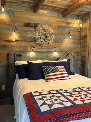 Una cama con colcha de estampado geométrico, una pared con diseño de tablones de madera y una guirnalda de luces.