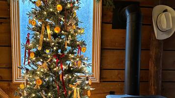 L’intérieur chaleureux d’un chalet avec un sapin de Noël décoré, un poêle à bois et une fenêtre offrant une belle vue.