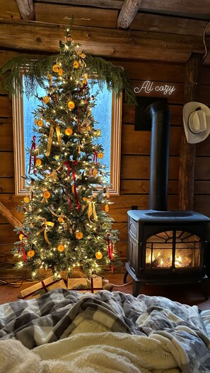Interior acogedor de una cabaña con un árbol de Navidad decorado, un hogar a leña y un ventanal con vistas.