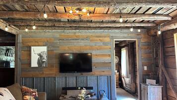 A rustic interior with exposed wooden beams, a television mounted on a wall, a sofa with decorative pillows, and a red throw blanket on the floor.
