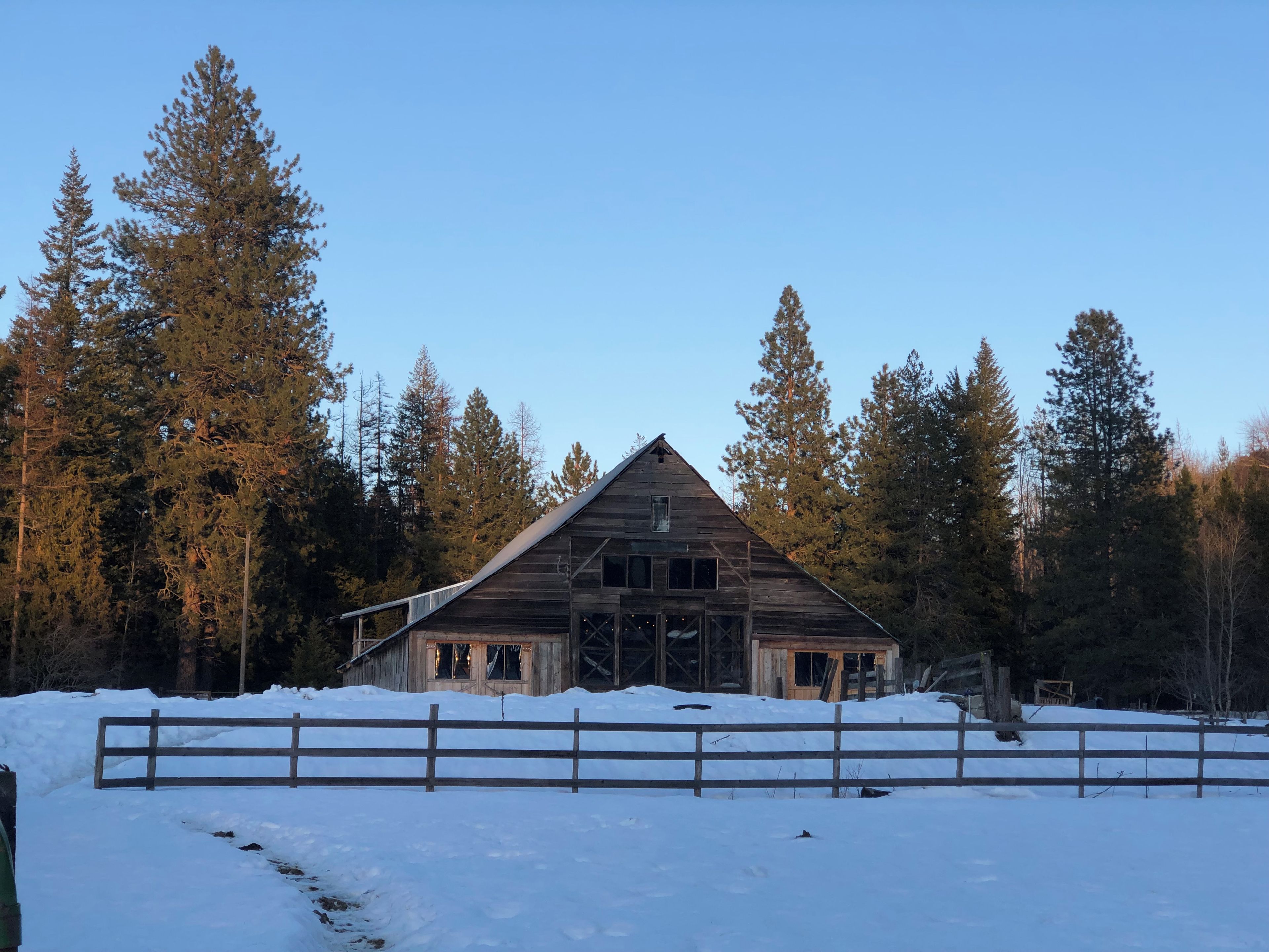 A rustic wooden barn surrounded by snow and tall pine trees.