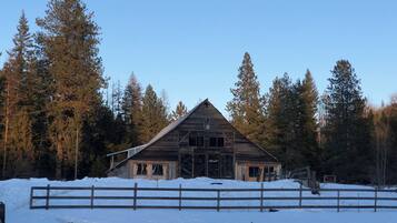 A rustic wooden barn surrounded by snow and tall pine trees.