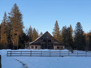 Un granero de madera rústico rodeado de nieve y altos pinos.