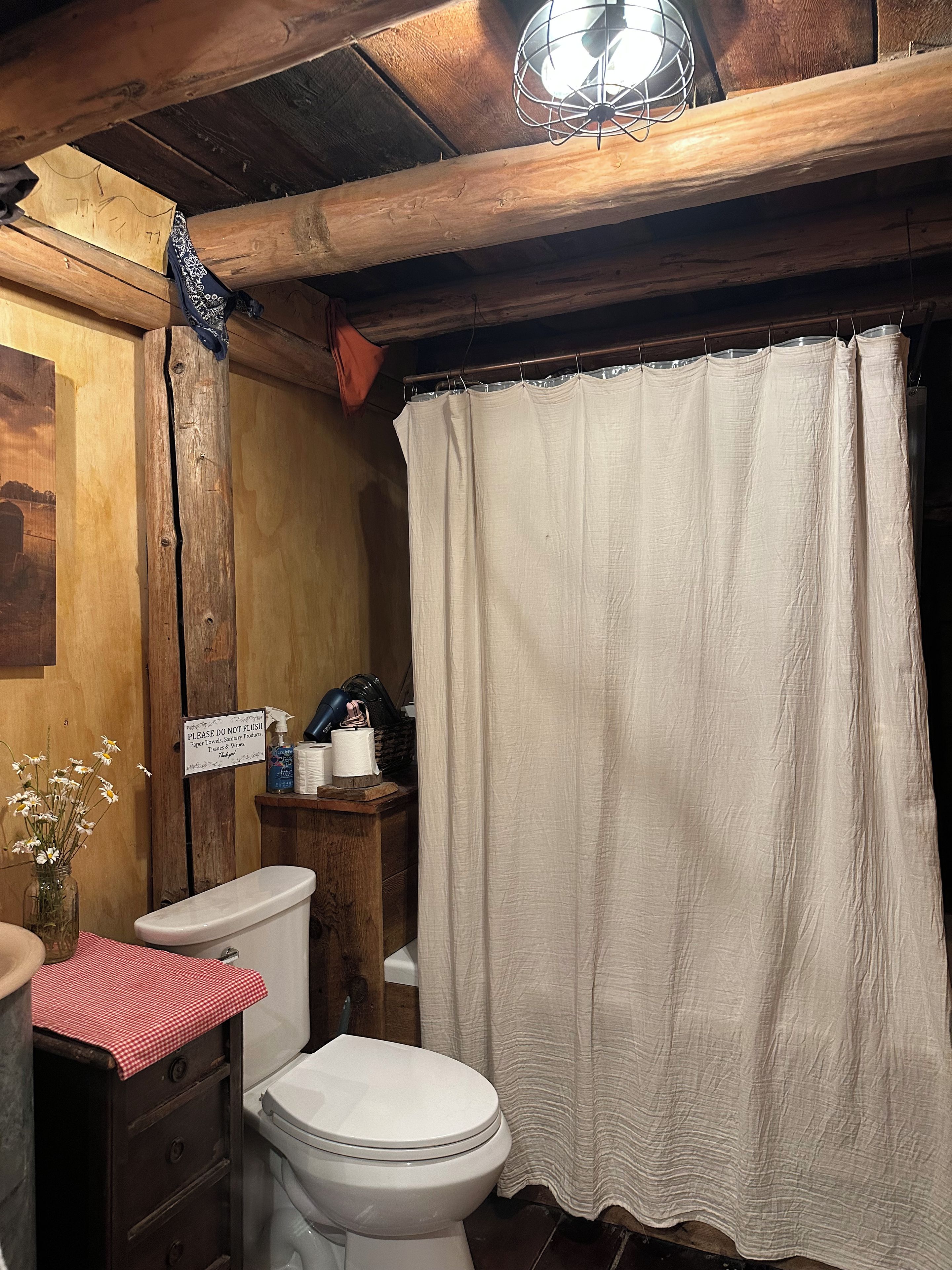 A rustic bathroom with a wooden ceiling, a white toilet, a wooden cabinet, and a shower curtain.