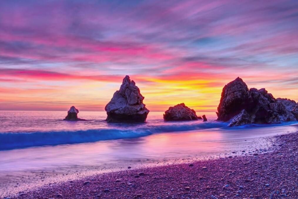 Ein Strand mit großen Felsformationen und einem Sonnenuntergang.
