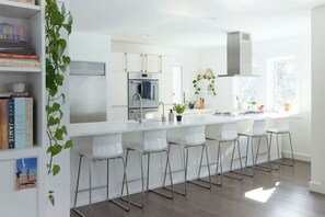 Une cuisine moderne avec des meubles blancs, une hotte en acier inoxydable et un îlot central doté de tabourets de bar.