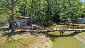 Un pont de fusta que uneix una cabana a un estany en una zona boscosa.