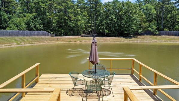 A wooden deck with a glass table and chairs, overlooking a calm body of water.