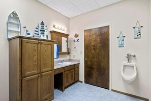 Un bany amb armaris de fusta, un lavabo, un mirall, una porta i un vàter.