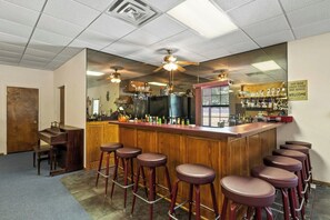 Een bar met een houten toonbank, meerdere krukken en een grote spiegel die de bar weerspiegelt.