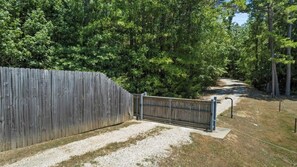 Une clôture en bois avec un portail, un chemin de gravier et une zone boisée.
