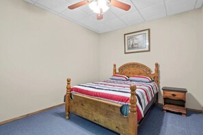 Een slaapkamer met een houten bed, een nachtkastje, een plafondventilator en een ingelijste foto aan de muur.