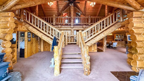 A log cabin interior with a central staircase, wooden walls, and a ceiling fan.