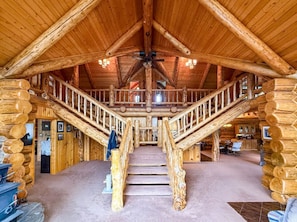 L’intérieur d’une cabane en rondins, avec un escalier central, des murs en bois et un ventilateur de plafond.