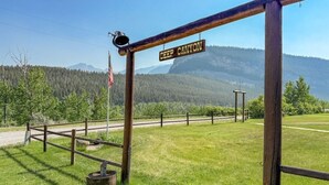 A wooden signpost with 'DEEP CANYON' written on it, a flagpole with an American flag, and a fenced area with a clear view of a forested mountain range.