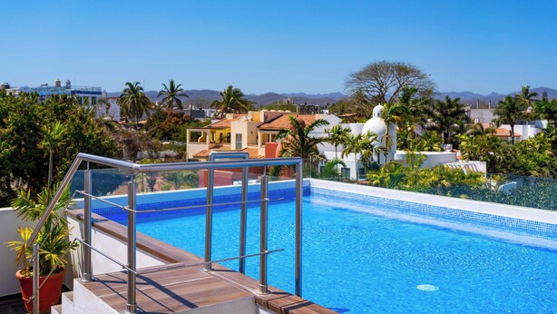 Una piscina con cielo azul despejado, palmeras y montañas a lo lejos.