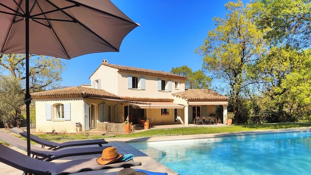 Una casa con piscina, sillas de descanso y una sombrilla.