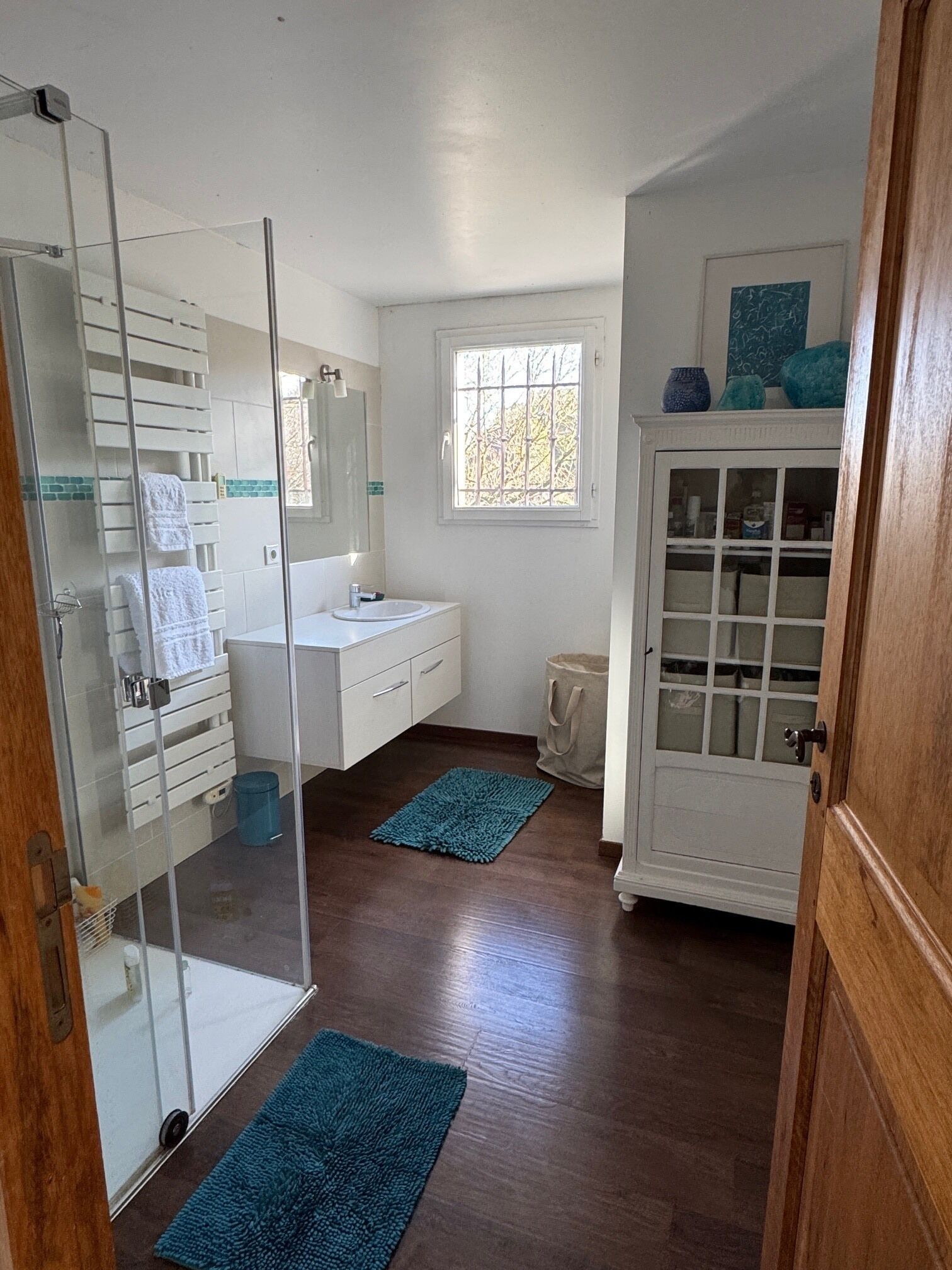 Une salle de bain avec une porte de douche en verre, un meuble-lavabo blanc et une fenêtre.