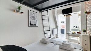 A modern bedroom with a bed, a ladder, a desk, and a bathroom visible through an open door. - APPARTEMENT PARIS 10eme CANAL ST MARTIN (Paris)