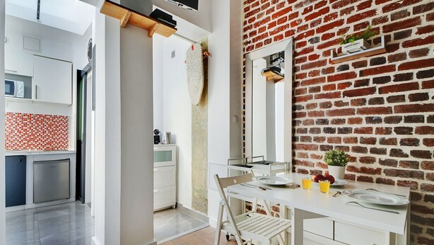 A modern kitchen with white cabinets, a dining area with a white table and chairs, and a brick wall. - APPARTEMENT PARIS 10eme CANAL ST MARTIN (Paris)