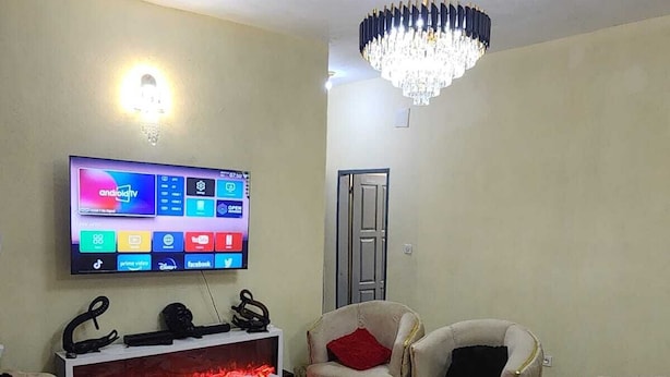Una sala de estar con un televisor de pantalla plana, una chimenea, dos sillones, una mesa redonda de centro y una araña.