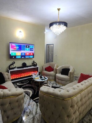 Una sala de estar con un televisor de pantalla plana, una chimenea, dos sillones, una mesa redonda de centro y una araña.