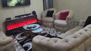 Una sala de estar con una televisión de pantalla plana, chimenea, dos sillones, un sofá y una mesita redonda.