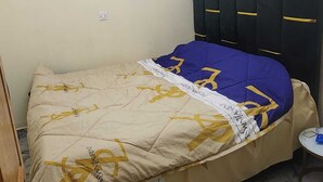 Un dormitorio con cama, cabecera, una mesita y una puerta.