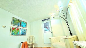 A room with a white ceiling, a door with a window, a chair, a sofa, and a table with a lamp. - Cozy haven (Toronto)