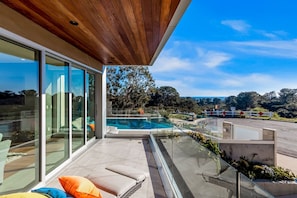 Una casa moderna con balcón de cristal, piscina y vistas al paisaje.