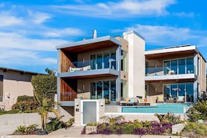 Una casa moderna de dos pisos con piscina, ventanas amplias y un jardín cuidado.