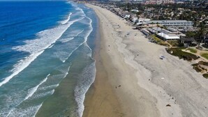 A coastal beach with a long stretch of sand, a few buildings, and a clear view of the ocean.