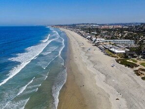 A coastal beach with a long stretch of sand, a few buildings, and a clear view of the ocean.