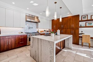Una cocina moderna con una isla de mármol, electrodomésticos de acero inoxidable, armarios de madera, luces colgantes y salpicadero de azulejos.