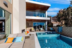 A modern two-story house with a swimming pool, outdoor seating, and a view of the surrounding area.