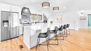 A modern kitchen with stainless steel appliances, a central island with bar stools, pendant lighting, and a view to the living area. - Covered Dock, 2 Game Rooms, Kayaks, Firepit (Mooresville)