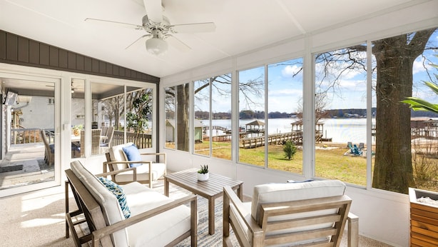 A sunroom with a view of a dock and lake, furnished with wooden chairs and a table. - Covered Dock, 2 Game Rooms, Kayaks, Firepit (Mooresville)