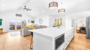 A modern kitchen with a central island, a dining area, and a living space with a sofa and a view through the glass doors. - Covered Dock, 2 Game Rooms, Kayaks, Firepit (Mooresville)
