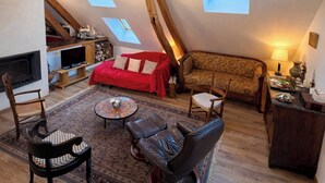 A loft-style living room with a fireplace, a red sofa, a patterned sofa, a leather chair, a small table, and a ceiling with wooden beams and a deer antler decoration. - 6-person apartment near La Motte Beuvron with box and paddock (Souesmes)