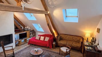 Ein Loft-Wohnzimmer mit Kamin, einem roten Sofa, einem gemusterten Sofa, einem Ledersessel, einem kleinen Tisch und einer Decke mit Holzbalken und einer Hirschgeweih-Dekoration.