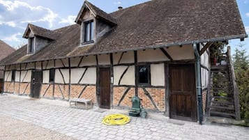 Ein traditionelles Fachwerkhäuschen mit einem Kieshof, Holzbanken und einem gelben Gartenschlauch auf dem Boden.
