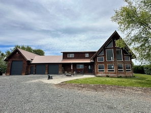 A two-story wooden building with multiple garage doors, a covered patio area, and a well-maintained lawn.