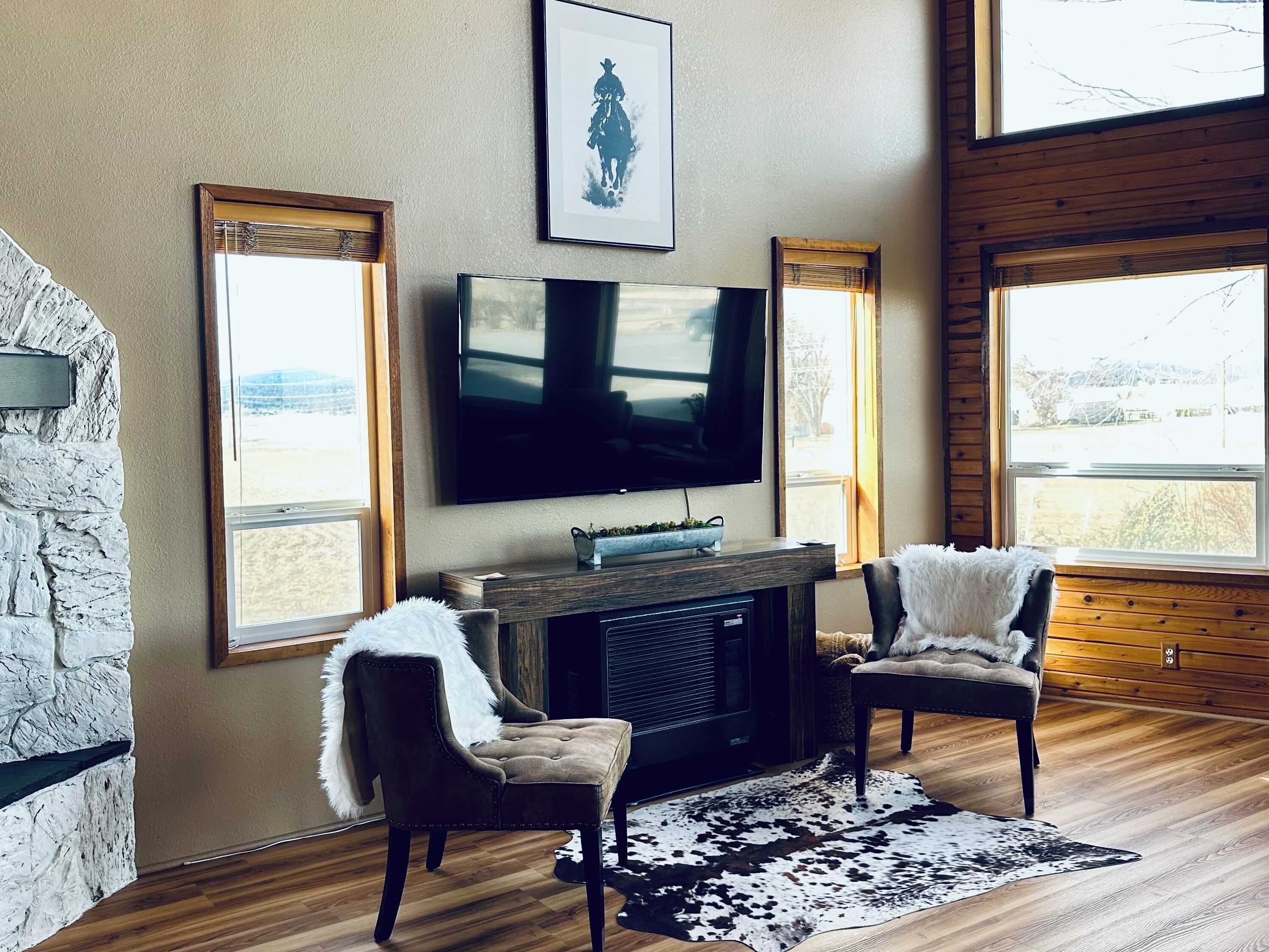 Un salon avec une cheminée, un téléviseur fixé au mur et deux fauteuils recouverts de plaids en fourrure.