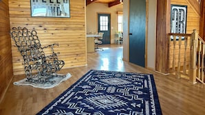 A wooden interior hallway with a 'HELLO' sign, a patterned rug, and a metal chair.