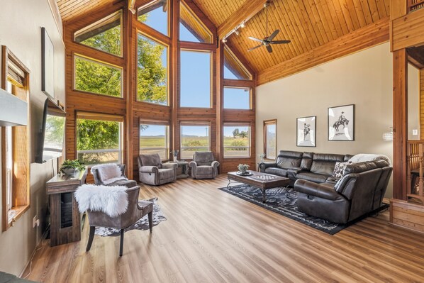 A spacious living room with large windows, a ceiling fan, and a fireplace.