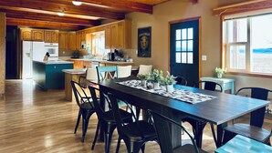 A spacious kitchen with wooden cabinets and a large island, a dining area with a long table and chairs, and a view through a window.