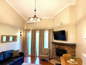 A living room with a sofa, armchair, fireplace, TV, and large windows with curtains.