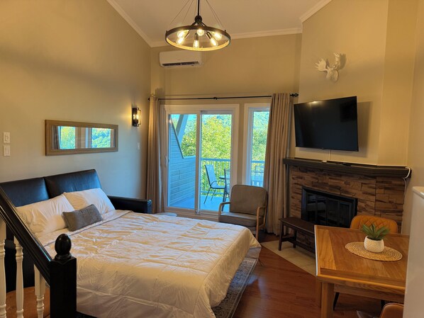 Un dormitorio con cama, televisor, chimenea y balcón con mobiliario exterior.