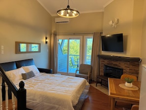 A bedroom with a bed, a TV, a fireplace, and a balcony with outdoor furniture.